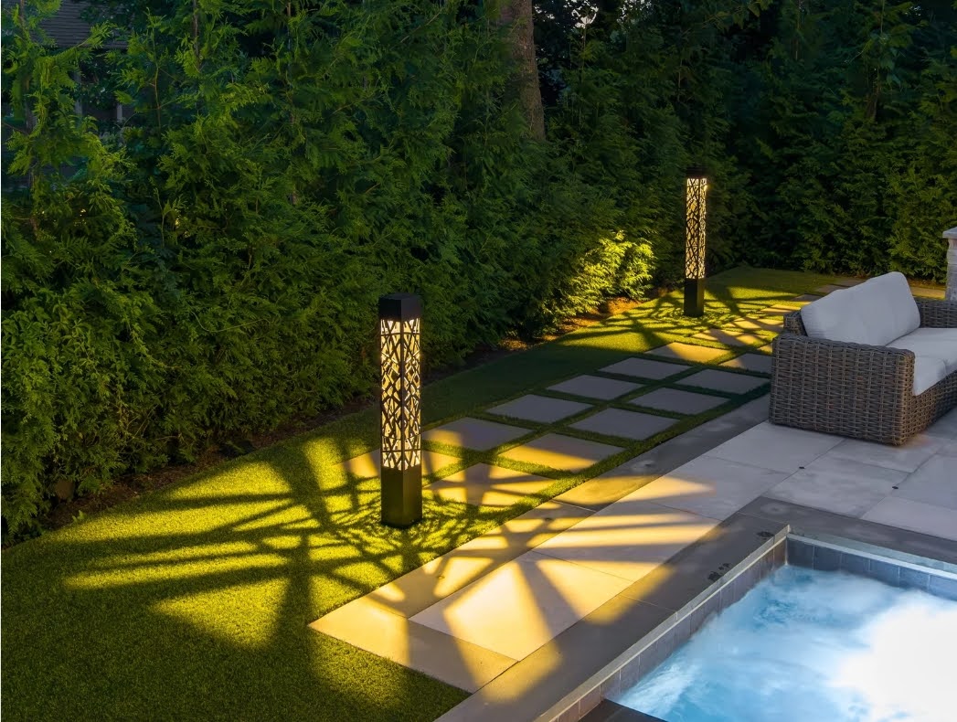 Two decorative lights beside stepping stones, evergreen planting, seating and a pool edge.